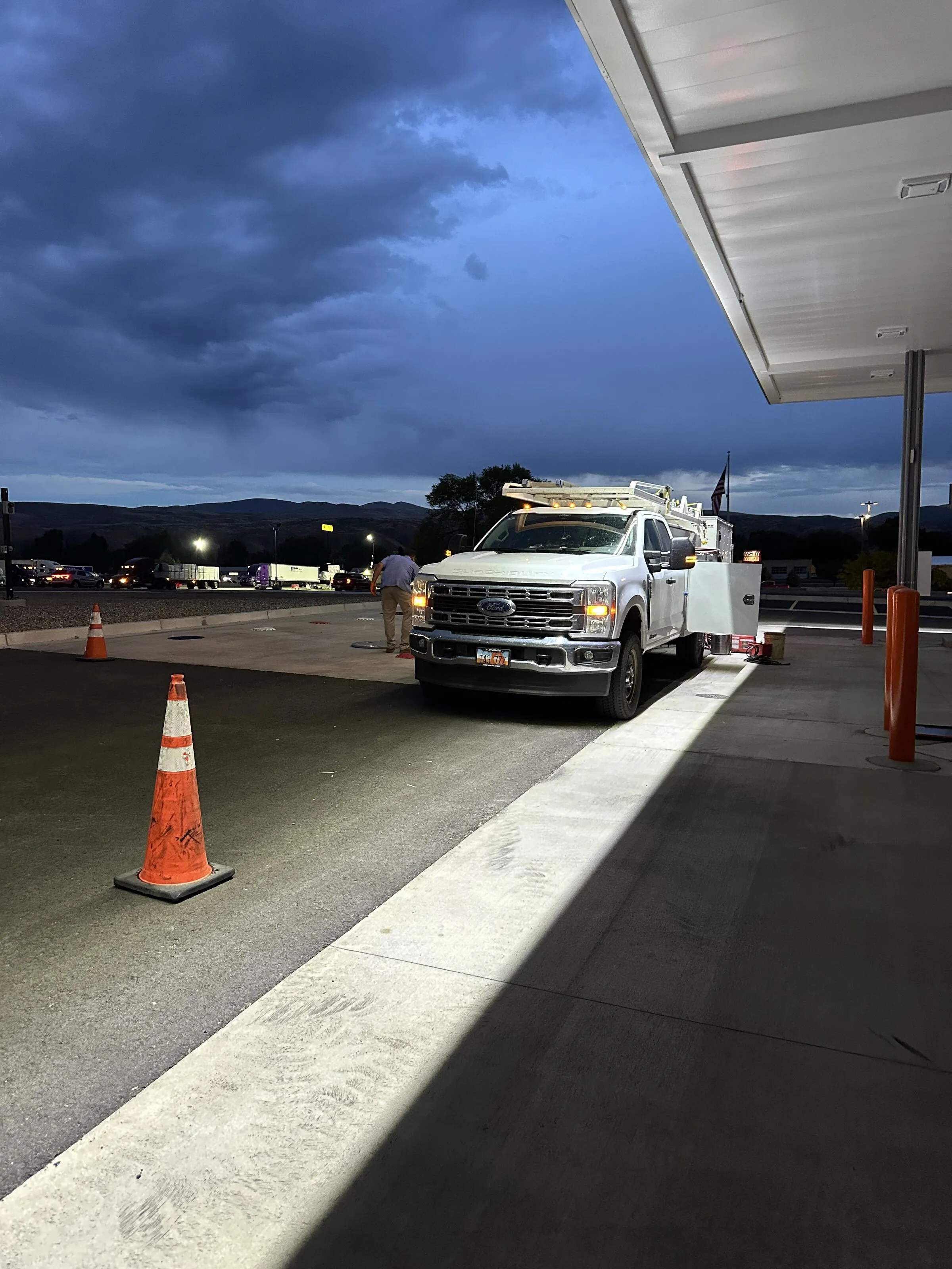 PTTI service truck parked under a fueling canopy at dusk with a technician approaching, dramatic stormy sky overhead in the Intermountain West.